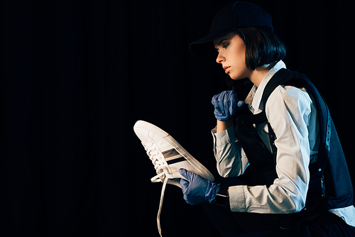 pensive investigator in uniform holding shoe isolated on black