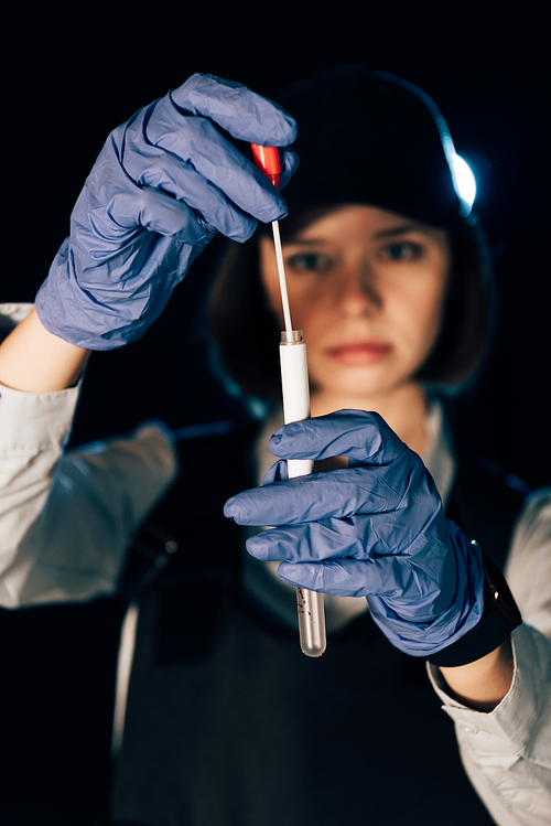 selective focus of investigator in rubber gloves holding swab and test tube at crime scene