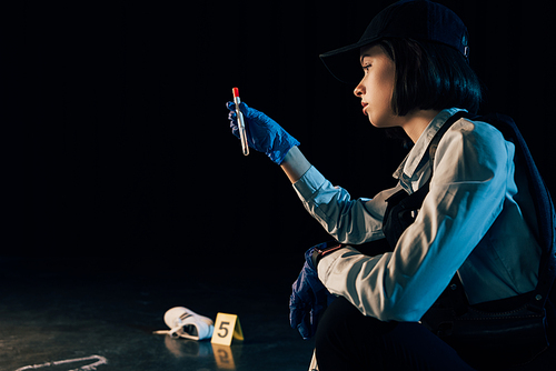 pensive investigator in rubber gloves holding test tube at crime scene