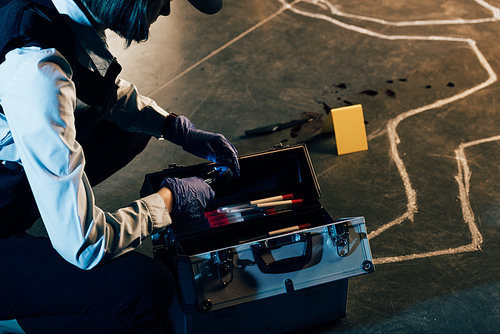 cropped view of investigator in rubber gloves with investigation kit at crime scene