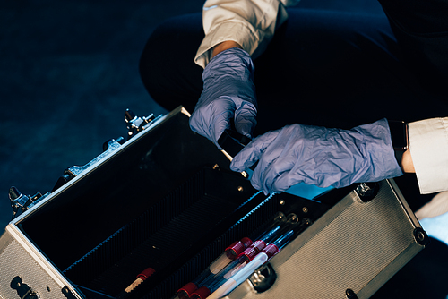 cropped view of investigator in rubber gloves with investigation kit at crime scene