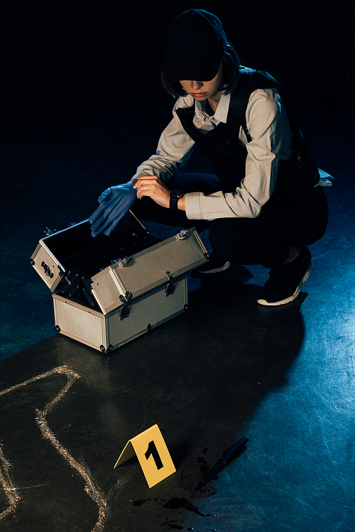 investigator with investigation kit putting on rubber glove at crime scene