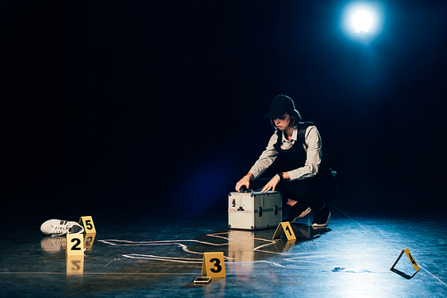 investigator with investigation kit near chalk outline at crime scene