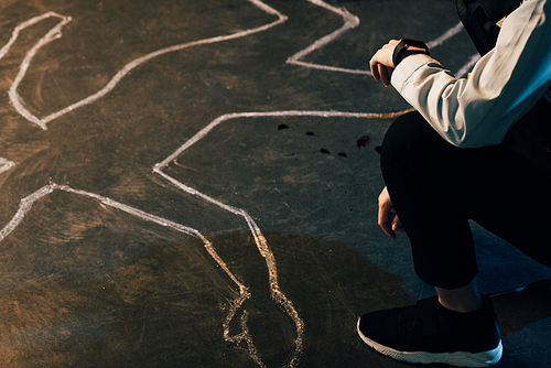 partial view of investigator sitting near chalk outline at crime scene