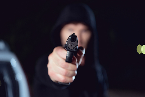 selective focus of gun in hand of thief in black hoodie