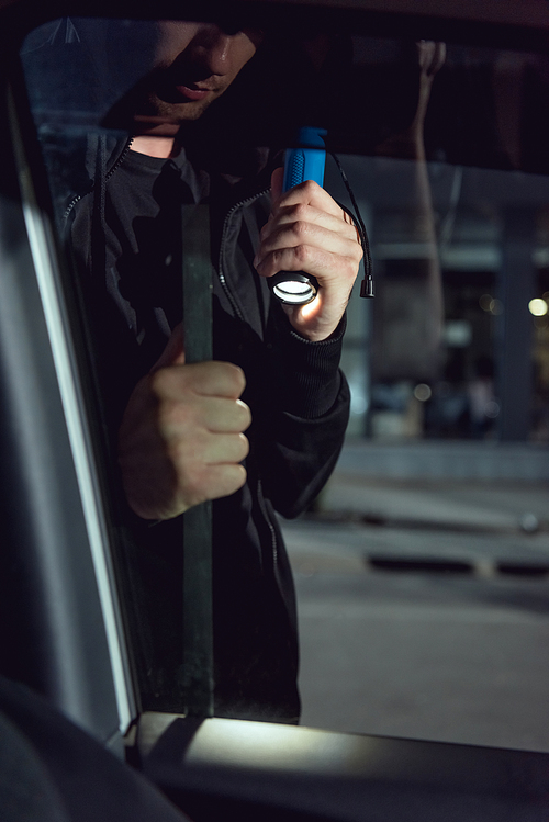 cropped view of thief intruding car with flashlight and crowbar