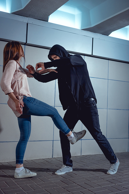 woman defending herself from attacking thief in black hoodie in underpass