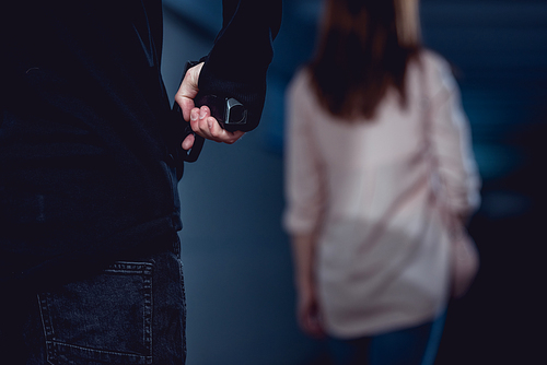 selective focus of robber holding gun behind walking woman