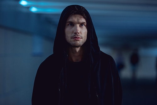 selective focus of handsome thief in black hoodie in underpass