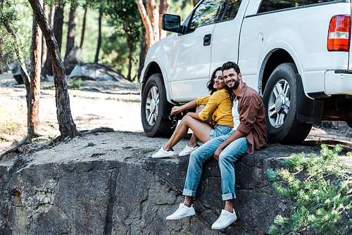 happy bearded man and attractive woman sitting near car and trees