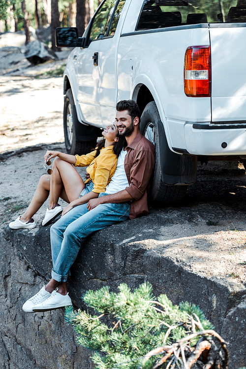 happy bearded man and attractive woman sitting near car