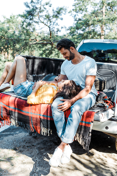 handsome bearded man smiling while cheerful girl lying on plaid blanket