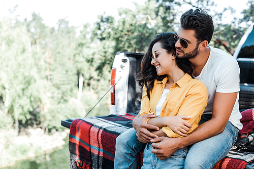 handsome bearded man hugging beautiful girl in sunglasses near car