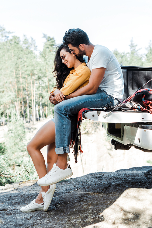 bearded man hugging attractive girl in sunglasses near automobile