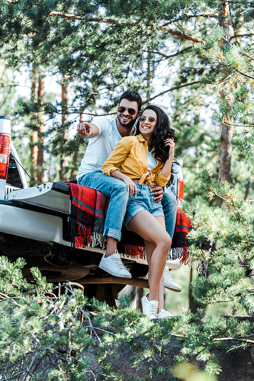 selective focus of cheerful bearded man pointing with finger near woman in sunglasses