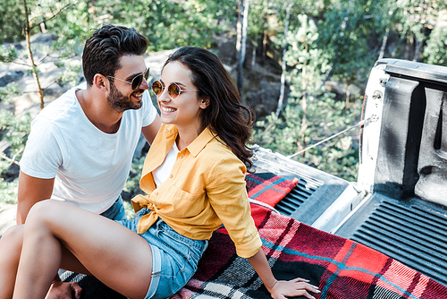 happy bearded man smiling with young woman sitting on blanket in summertime