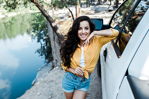 selective focus of happy girl smiling while standing near car in woods
