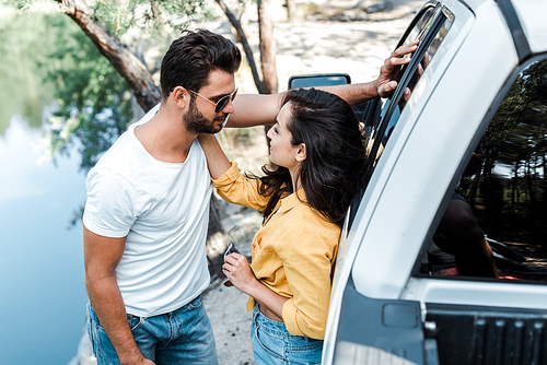 attractive girl in sunglasses touching face of bearded man near car