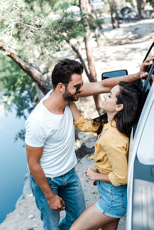 happy woman touching face of bearded man while standing near car