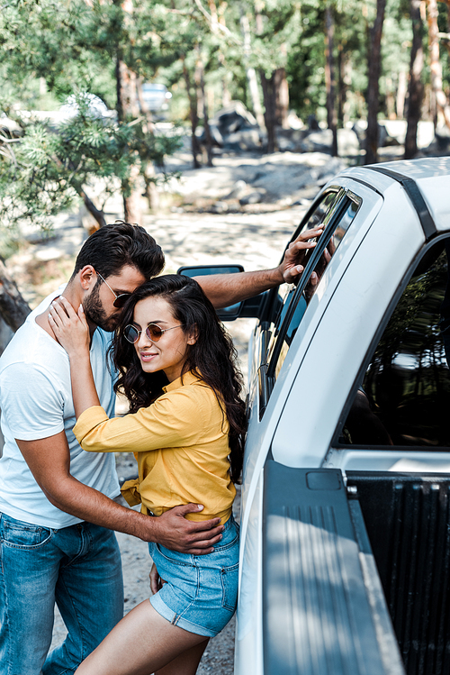 attractive girl in sunglasses hugging bearded man near car
