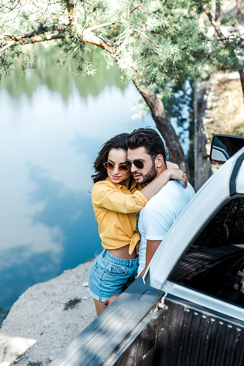 overhead view of woman hugging boyfriend near automobile and lake