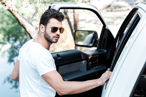 selective focus of bearded man in sunglasses standing near car