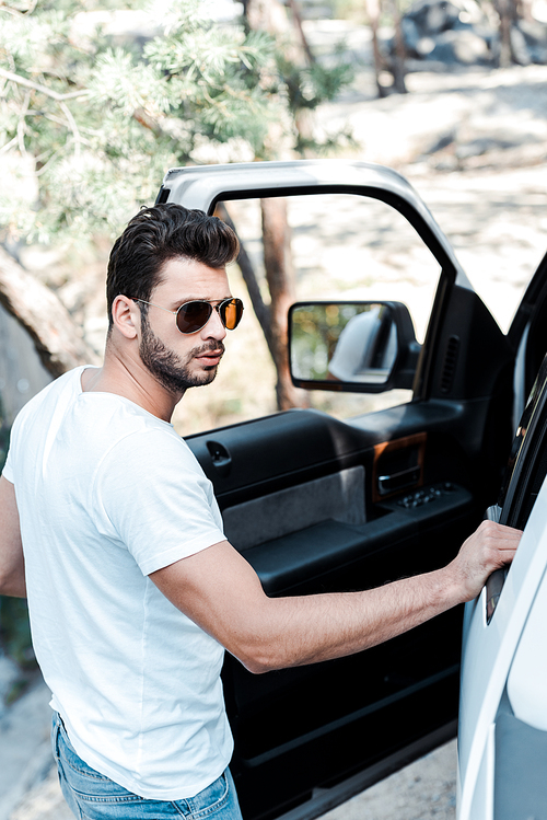 selective focus of handsome man in sunglasses standing near car