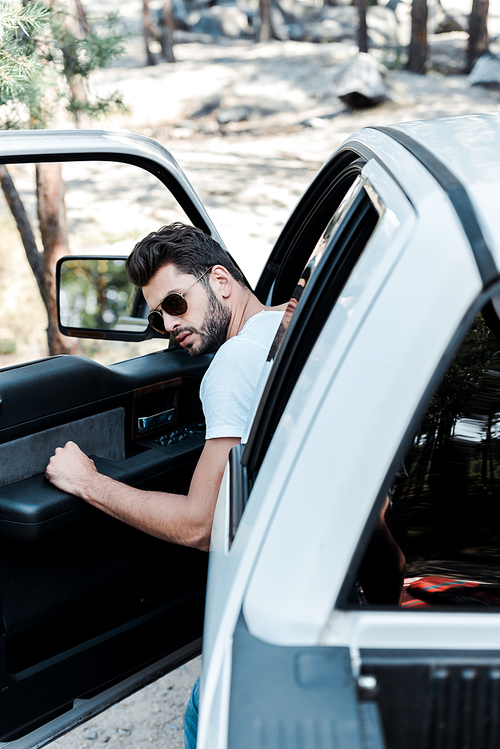 selective focus of man in sunglasses opening car door