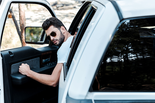 selective focus of bearded man in sunglasses opening car door