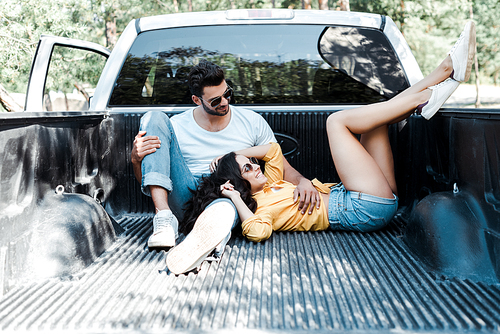 cheerful man in sunglasses sitting in car trunk near girl