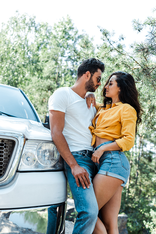 handsome man standing and hugging happy girl near auto in woods