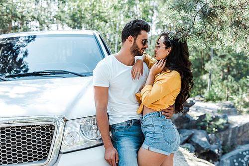 handsome man hugging attractive woman near auto in woods