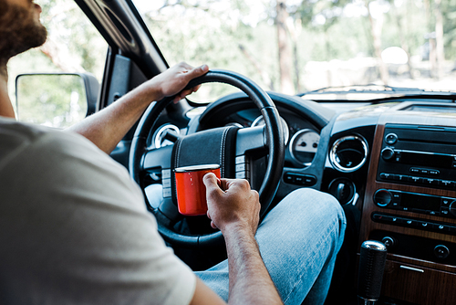 cropped view of bearded man holding cup and touching steering wheel