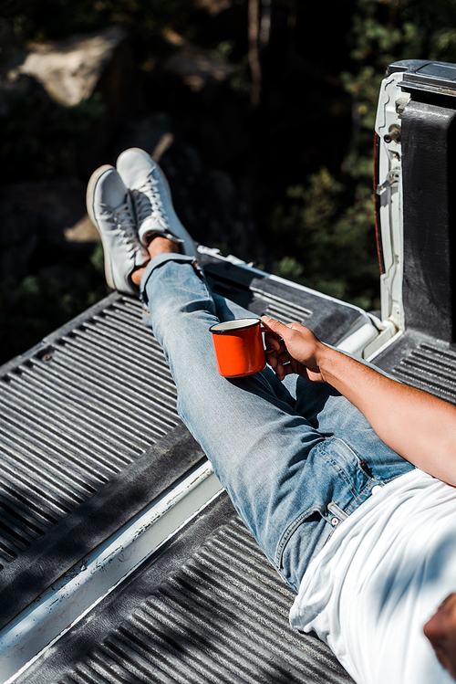 cropped view of man lying in car trunk and holding red cup