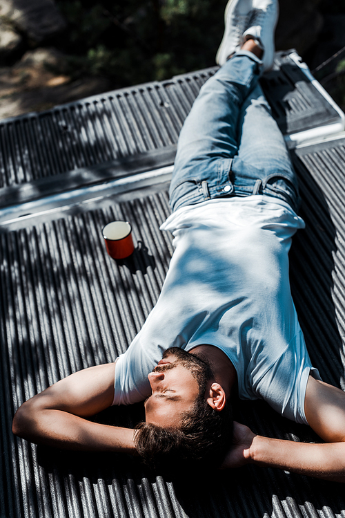 overhead view of bearded man lying with closed eyes near cup