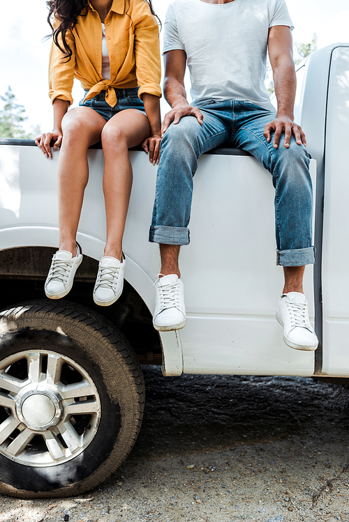cropped view of young man and woman sitting on car