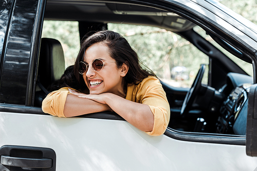 cheerful girl in sunglasses smiling from car window