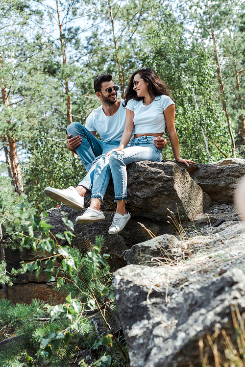 selective focus of man and woman sitting on rocks near trees