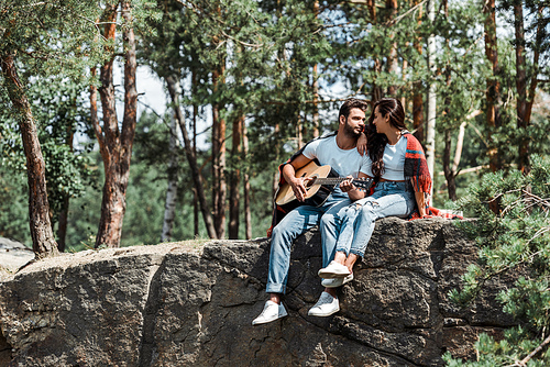 bearded man playing acoustic guitar near woman in woods