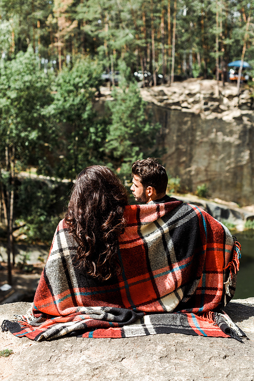 back view of girl and man wrapped in plaid blanket in woods