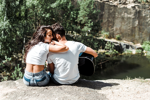 attractive girl sitting near man playing acoustic guitar in woods