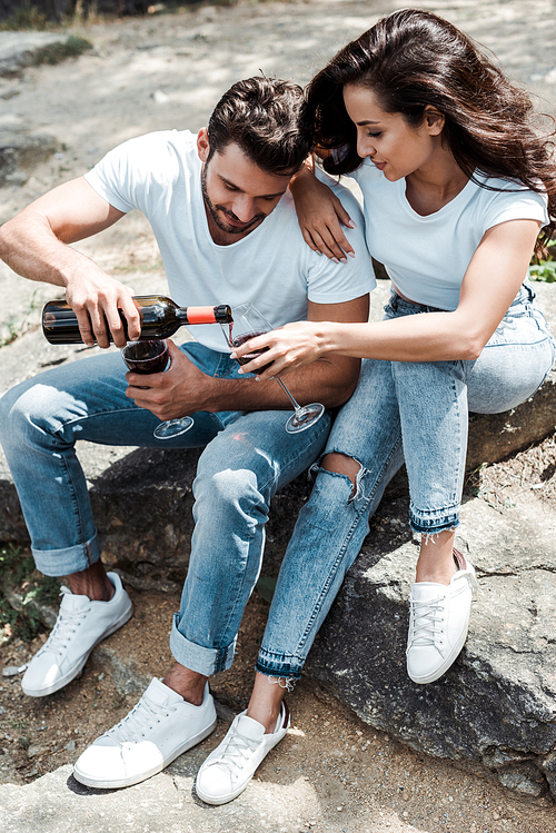 overhead view of man pouring red wine from bottle near woman