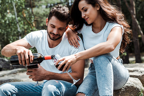 handsome man pouring red wine from bottle near attractive woman