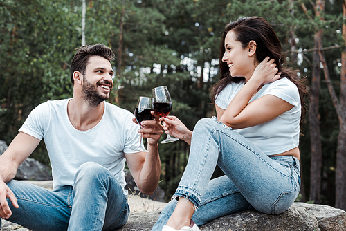 cheerful man and young woman clinking wine glasses in woods