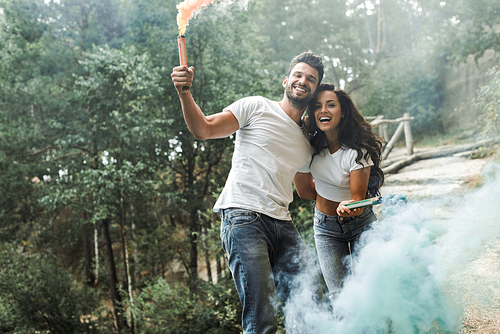 attractive woman and cheerful bearded man holding smoke bombs