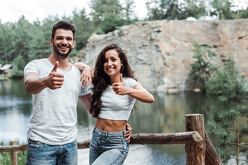 cheerful woman and happy man showing thumbs up near lake