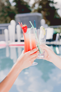 cropped view of women clinking with glasses of cocktail near swimming pool