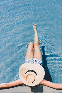overhead view of young woman in straw hat resting in swimming pool