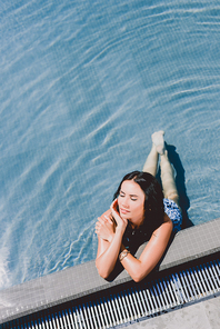 beautiful brunette wet woman with closed eyes sunbathing in water in swimming pool