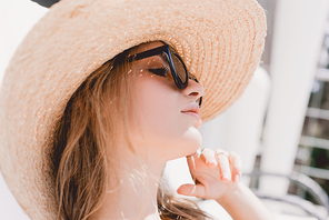 portrait of attractive dreamy blonde woman sunbathing in sunglasses and straw hat